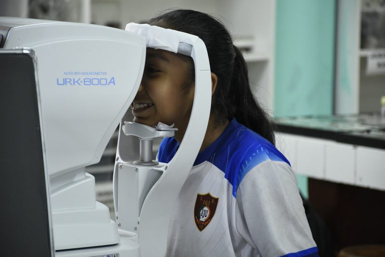 Ein Kind sitzt an einem Auto‑Refraktometer und erhält eine augenoptische Untersuchung.